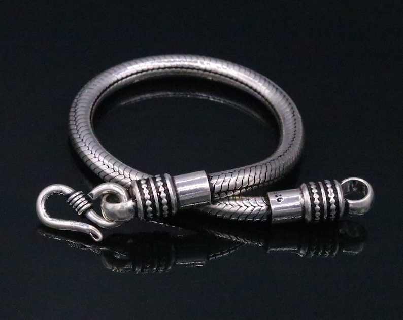 K&ouml;nnte beinhalten: Ein silbernes Schlangenkettenarmband mit einem Hakenverschluss. Das Armband ist etwa 19 cm lang.