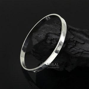 Puede incluir: Un brazalete de plata con acabado martillado. El brazalete está sobre un fondo negro.