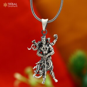 May include: A silver pendant necklace with a detailed depiction of a multi-armed deity. The pendant hangs from a silver chain. The image has the text "TRIBAL Ornaments" in the upper left corner. The background is a gradient of red and orange.