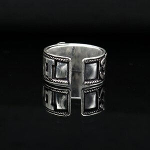 May include: Silver ring with a square design and intricate details. The ring is open on one side, allowing it to be adjusted to fit different finger sizes.