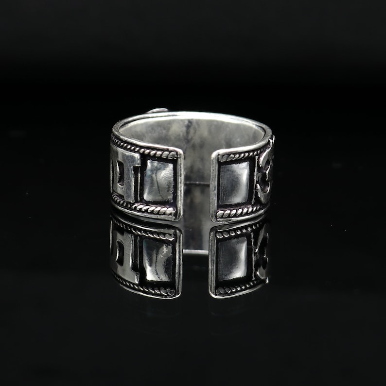 May include: Silver ring with a square design and intricate details. The ring is open on one side, allowing it to be adjusted to fit different finger sizes.
