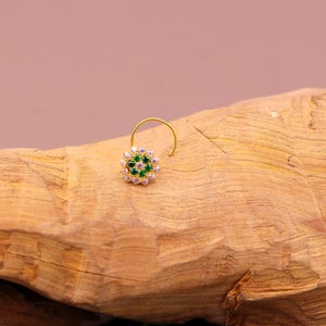 May include: A gold nose ring with a round design featuring green and white stones.