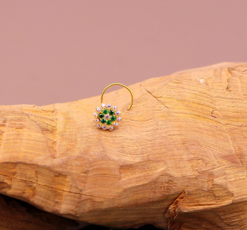 May include: A gold nose ring with a round design featuring green and white stones.