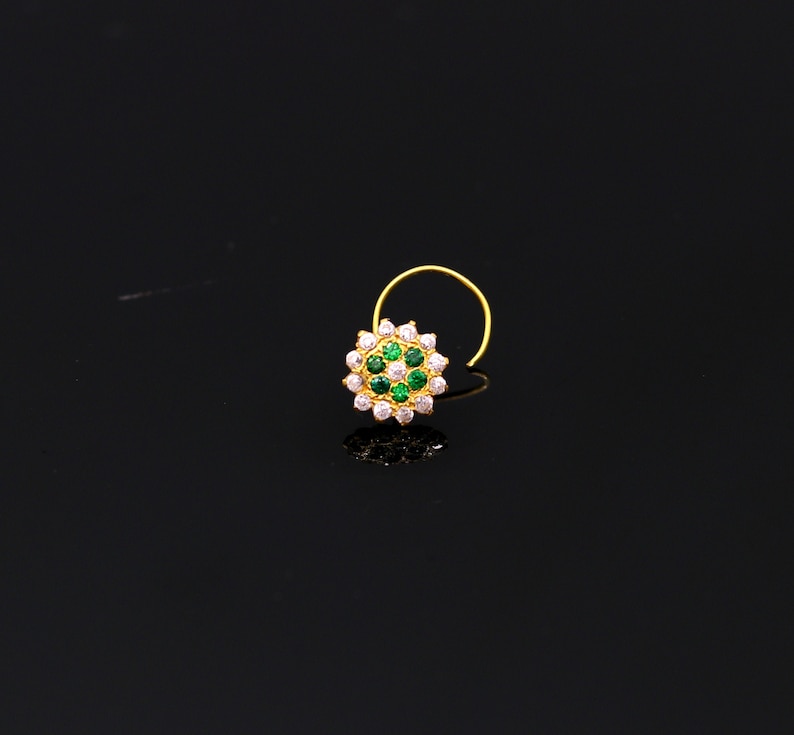 May include: A gold nose ring with a circular design featuring green and white gemstones.