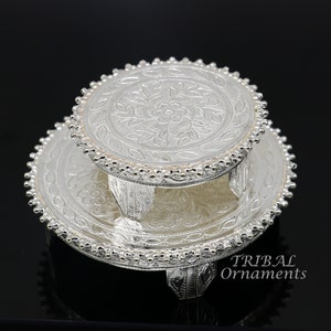 Puede incluir: Un soporte de plata de dos niveles con intrincados diseños florales y bordes con cuentas. El soporte tiene cuatro patas y es perfecto para exhibir objetos pequeños.