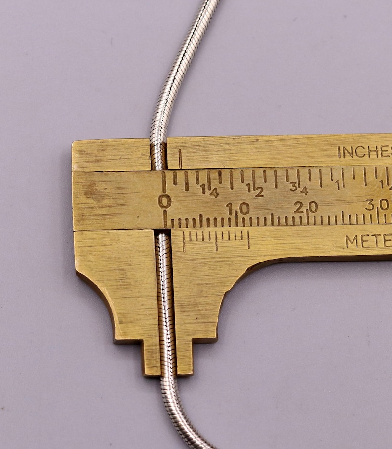 May include: A close-up of a silver snake chain being measured with a ruler. The ruler shows the chain is 2.5 cm long.