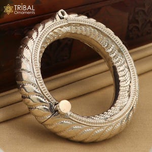May include: A silver bangle bracelet with intricate, detailed designs. The bracelet is hinged and opens to fit the wrist.