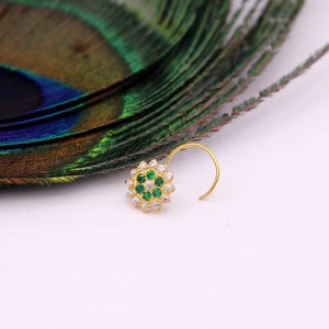 May include: A gold nose ring with a circular design featuring white and green gemstones.