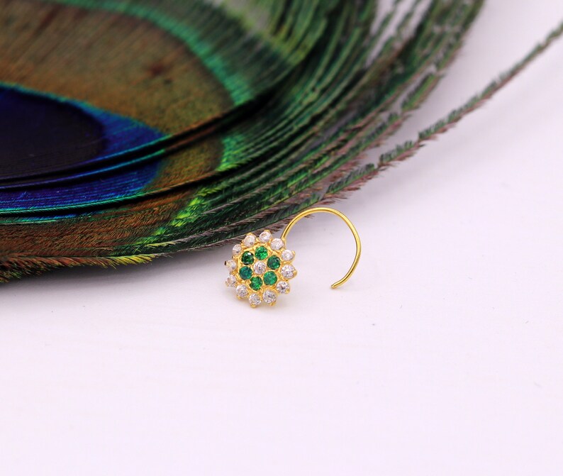 May include: A gold nose ring with a circular design featuring white and green gemstones.