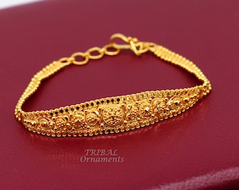 May include: A gold bracelet with a detailed design featuring a row of circular motifs. The bracelet has a clasp closure.