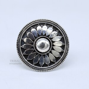 May include: A silver ring with a circular design featuring a central dome surrounded by a ring of petals. The ring has a textured, beaded edge.