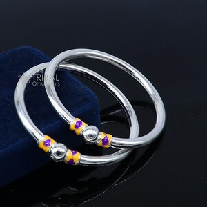 May include: Two silver bangles with purple and yellow enamel accents. The bangles are stacked on top of each other.
