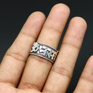 May include: Silver ring with a raised inscription of Sanskrit characters, including the Om symbol.