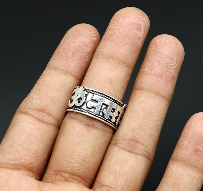 May include: Silver ring with a raised inscription of Sanskrit characters, including the Om symbol.
