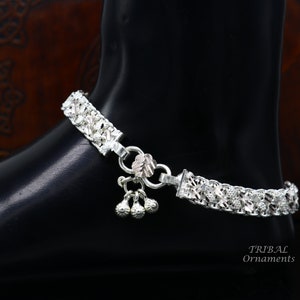 May include: Silver anklet with a delicate floral design and three small bells. The anklet is made of silver and has a floral pattern. The anklet is adorned with three small bells.