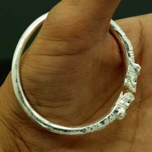 May include: Silver bangle bracelet with an intricate design featuring two stylized animal heads on the ends.