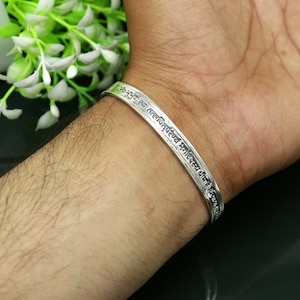 May include: Silver bracelet with an inscription in Sanskrit. The inscription is in a circular pattern around the bracelet.