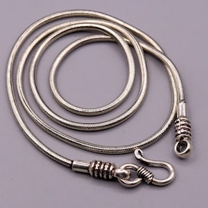 May include: A silver snake chain necklace with a clasp. The chain is approximately 20 inches long and features a delicate, textured design.