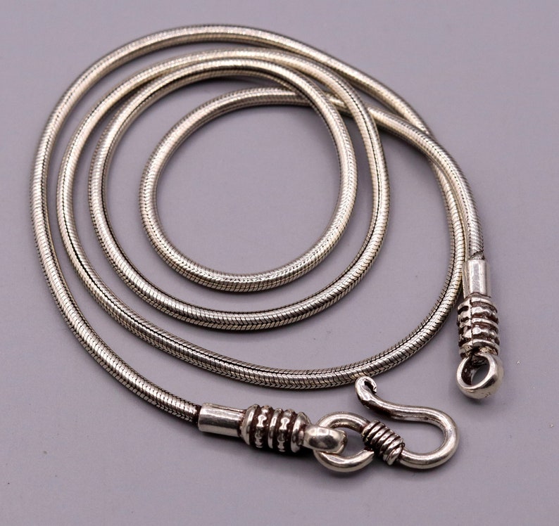 May include: A silver snake chain necklace with a clasp. The chain is approximately 20 inches long and features a delicate, textured design.