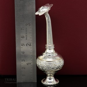 May include: A silver decorative bottle with a floral design and a spout shaped like a flower. The bottle is approximately 5 inches tall and is made in India.