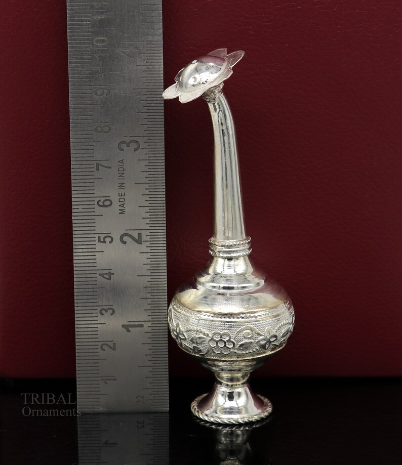 May include: A silver decorative bottle with a floral design and a spout shaped like a flower. The bottle is approximately 5 inches tall and is made in India.