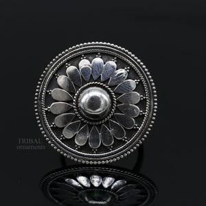 May include: A silver ring with a circular design featuring a central dome surrounded by a flower-like pattern of petals. The ring is made of sterling silver and has a traditional tribal design.