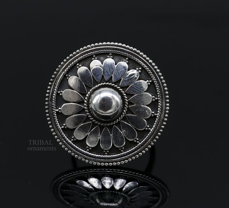 May include: A silver ring with a circular design featuring a central dome surrounded by a flower-like pattern of petals. The ring is made of sterling silver and has a traditional tribal design.