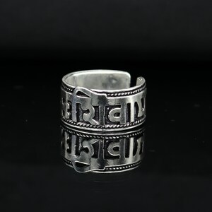 May include: Silver ring with an inscription in an ancient language. The ring is adjustable and has a simple design.