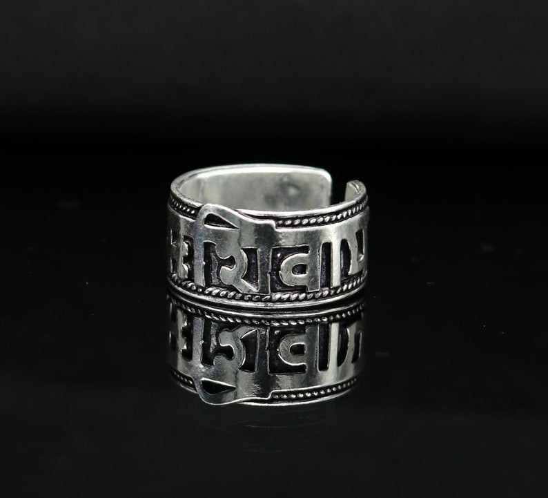 May include: Silver ring with an inscription in an ancient language. The ring is adjustable and has a simple design.