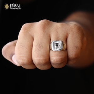 Może przedstawiać: Srebrny pierścionek z kwadratowym wzorem przedstawiającym słowo "राम" w języku hindi.