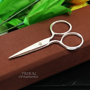 Puede incluir: Tijeras pequeñas plateadas sobre un fondo marrón. Las tijeras tienen un diseño sencillo con mangos redondeados.