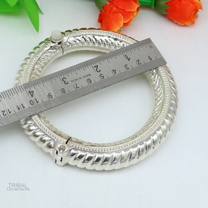 May include: Silver bangle bracelet with a twisted design and a hinged clasp. The bracelet measures approximately 5 cm in diameter.