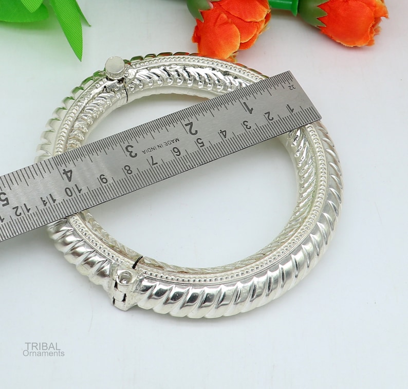 May include: Silver bangle bracelet with a twisted design and a hinged clasp. The bracelet measures approximately 5 cm in diameter.