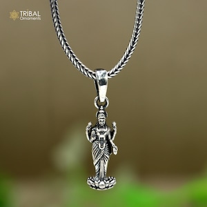 May include: Silver pendant necklace featuring a detailed depiction of the Hindu goddess Lakshmi, standing on a lotus flower. The necklace has a silver chain.
