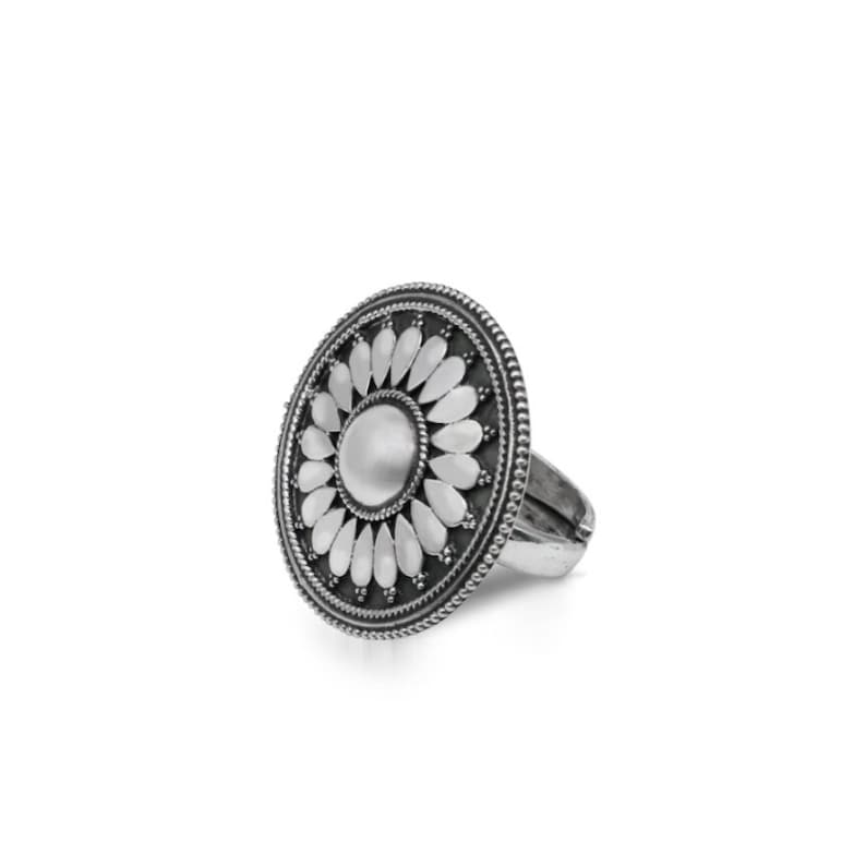 May include: A silver ring featuring a large, round, floral design. The ring is made of metal and has a detailed design of a flower with petals.