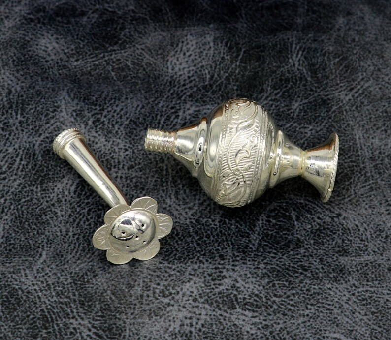 May include: Silver perfume bottle with a floral design and a separate nozzle. The nozzle has a flower-shaped end.