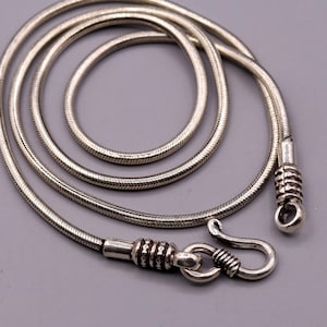 May include: A silver snake chain necklace with a hook clasp. The chain is made of small, round links that are tightly woven together.