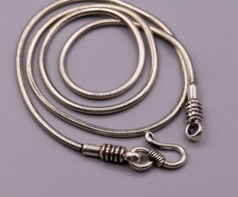 May include: A silver snake chain necklace with a hook clasp. The chain is made of small, round links that are tightly woven together.