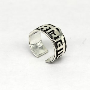 May include: Silver ring with an inscription in Sanskrit. The inscription is in black and the ring is adjustable.