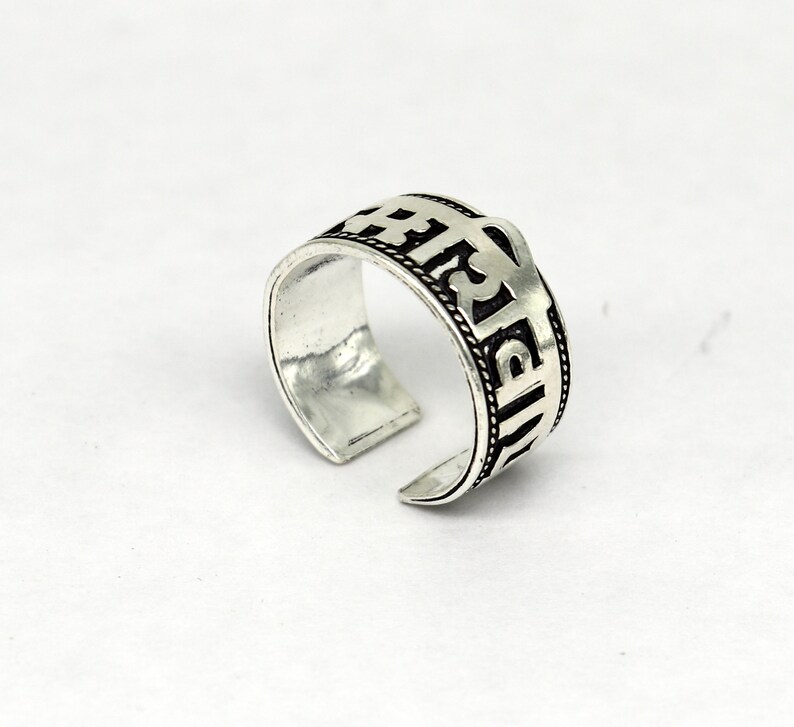 May include: Silver ring with an inscription in Sanskrit. The inscription is in black and the ring is adjustable.
