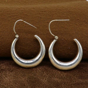 May include: A pair of silver hoop earrings with a smooth, rounded design. The earrings have a simple, elegant style.