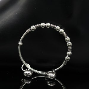 May include: A silver bracelet with a series of round beads and two dangling bells.