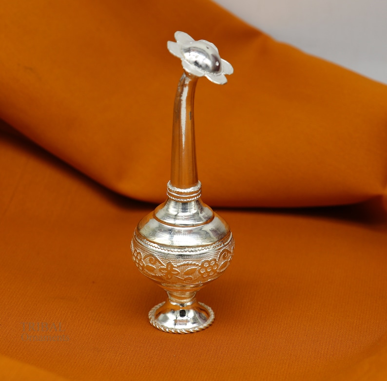 May include: A silver flower-shaped bottle with intricate floral designs. The bottle has a long, curved neck and a round base.