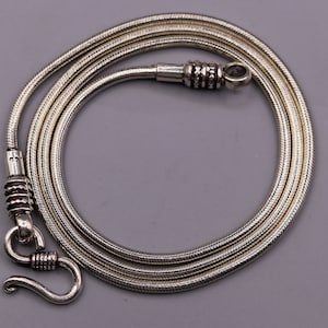 May include: A silver snake chain necklace with a clasp. The chain is approximately 20 inches in length.