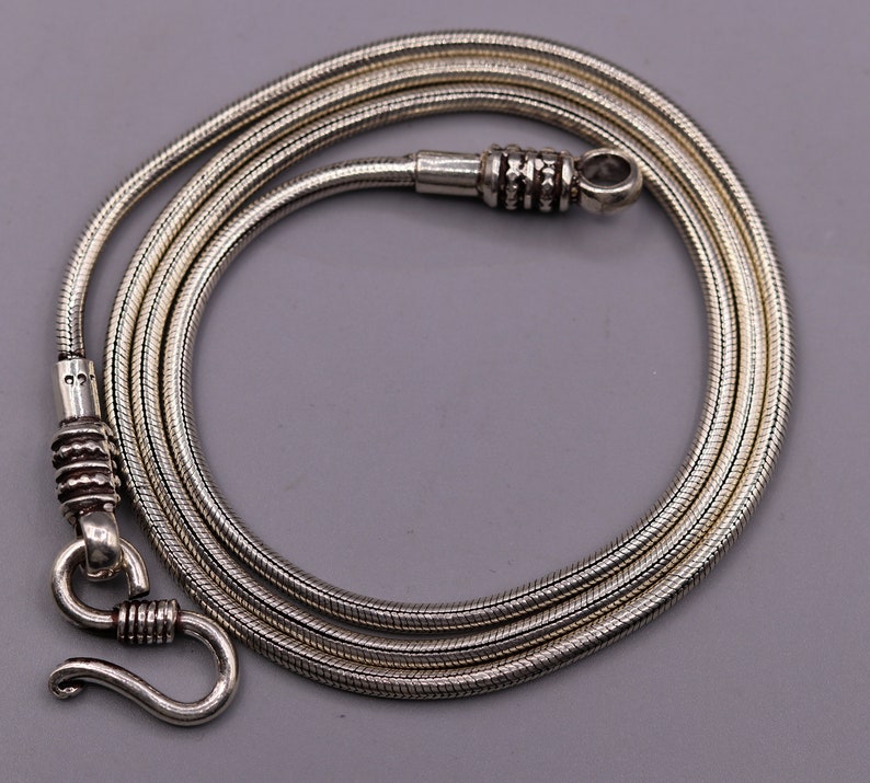 May include: A silver snake chain necklace with a clasp. The chain is approximately 20 inches in length.