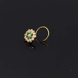 May include: A gold nose ring with a circular design featuring white and green gemstones.