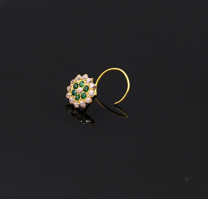 May include: A gold nose ring with a circular design featuring white and green gemstones.