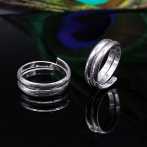 May include: Two silver toe rings with a simple, textured design. The rings are open and adjustable.