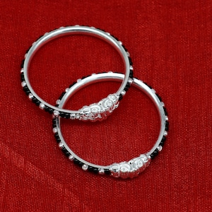 May include: Two silver bangles with black beads. The bangles are decorated with intricate silver designs.