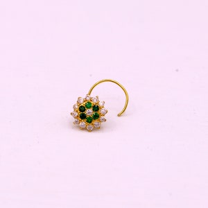 May include: A gold nose ring with a circular design featuring white and green gemstones.